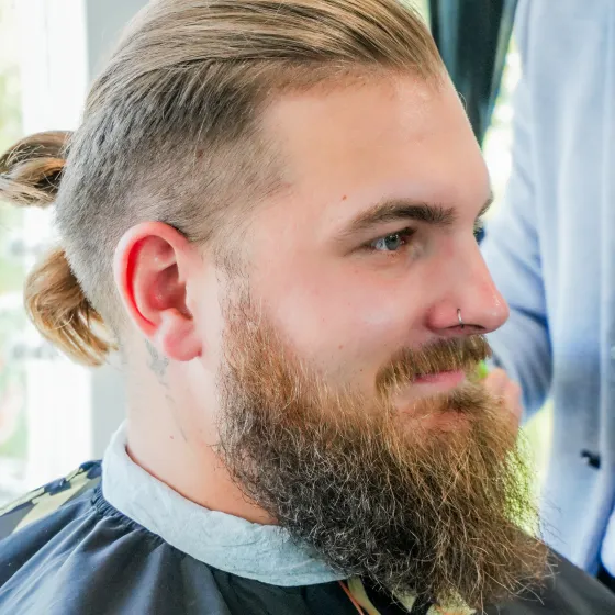 Close-up side profile of a man with a modern man-bun hairstyle, skin fade on the sides, and a groomed full beard.