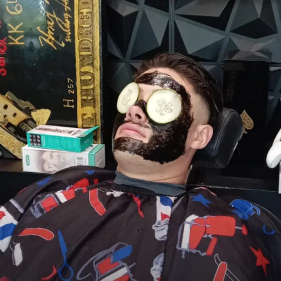 Barbershop client receiving a professional facial treatment with a black face mask and cucumber slices on eyes for relaxation.