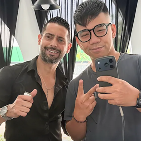 Happy client taking a mirror selfie next to a smiling barber holding hair clippers and giving a thumbs up.