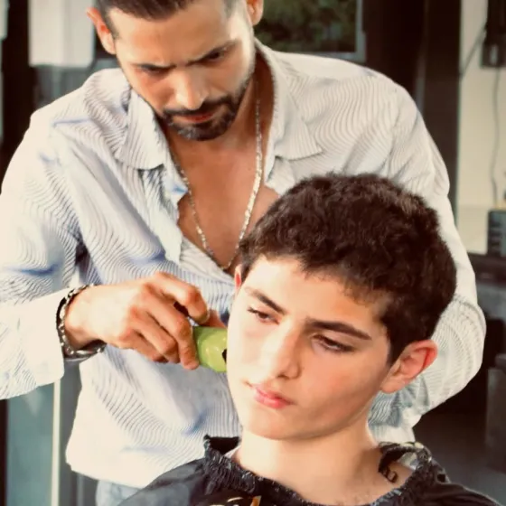 Professional barber cutting a young boy's hair using electric clippers, focusing on the side details.