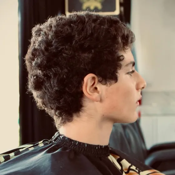 Side profile of a young man showing off a textured haircut for curly hair with a clean finish on the neckline.